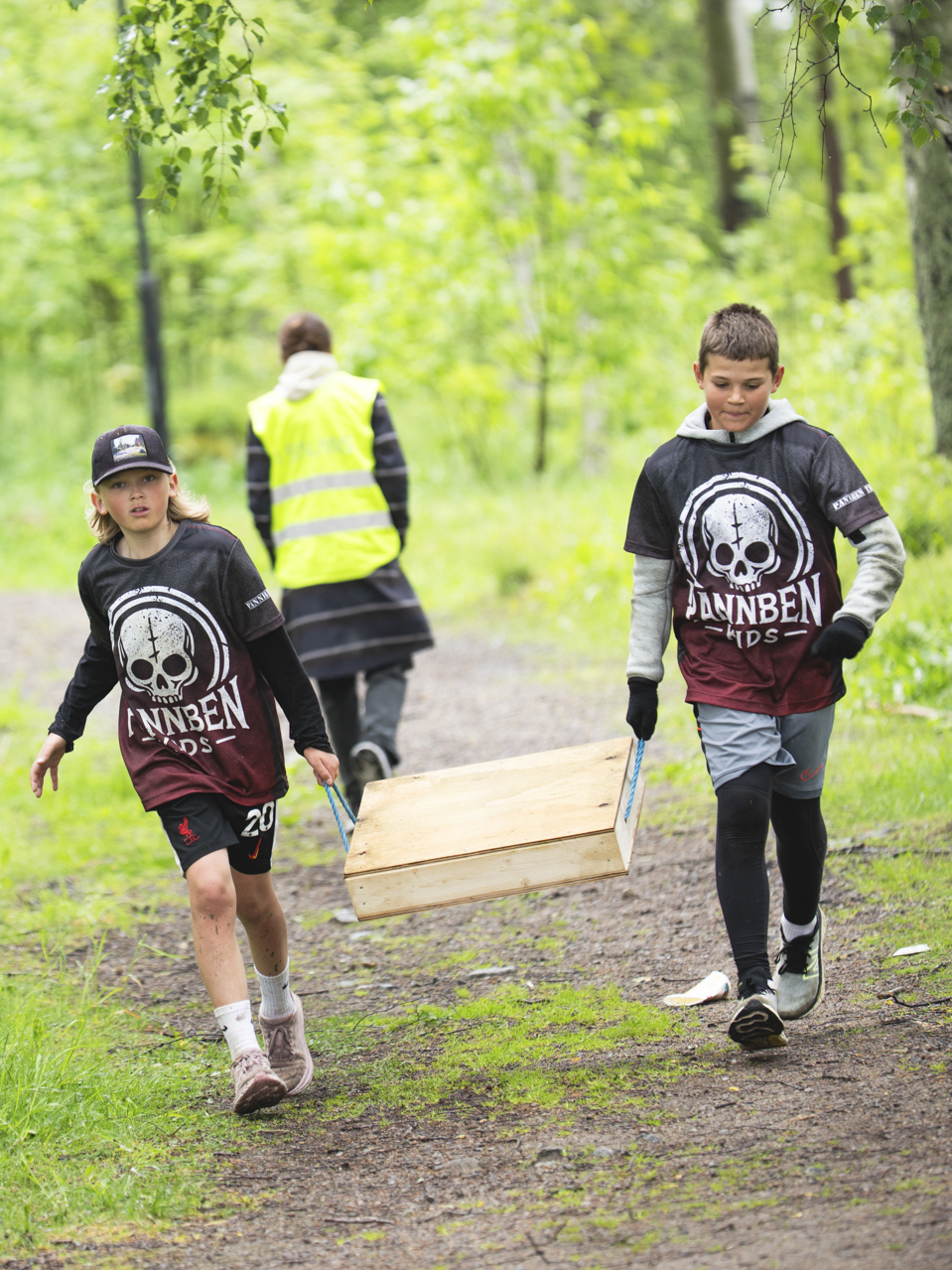 Två deltagare bär en låda genom skogsdelen av Pannben–Kids
