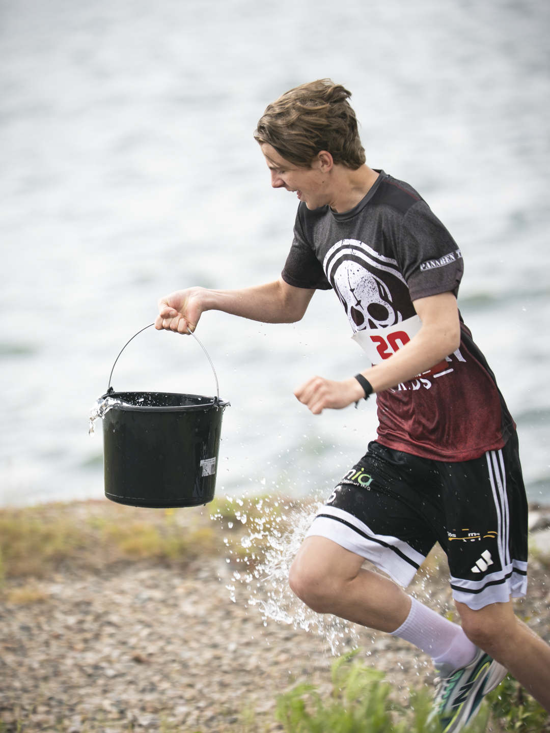 Deltagare springer med vattenhink vid strandkanten under Pannben–Kids