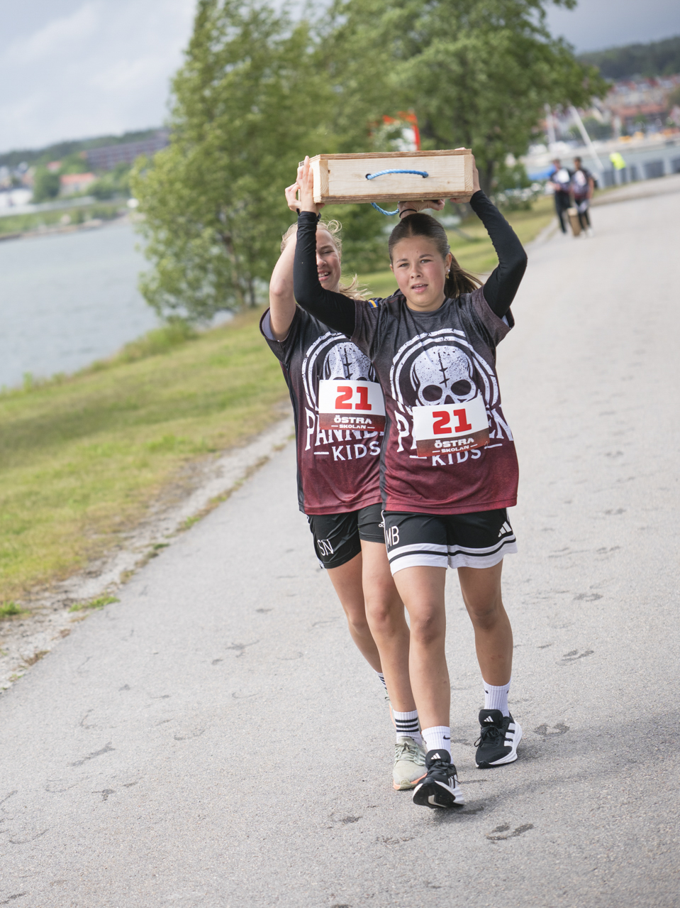 Två deltagare bär en låda längs strandpromenaden under Pannben–Kids